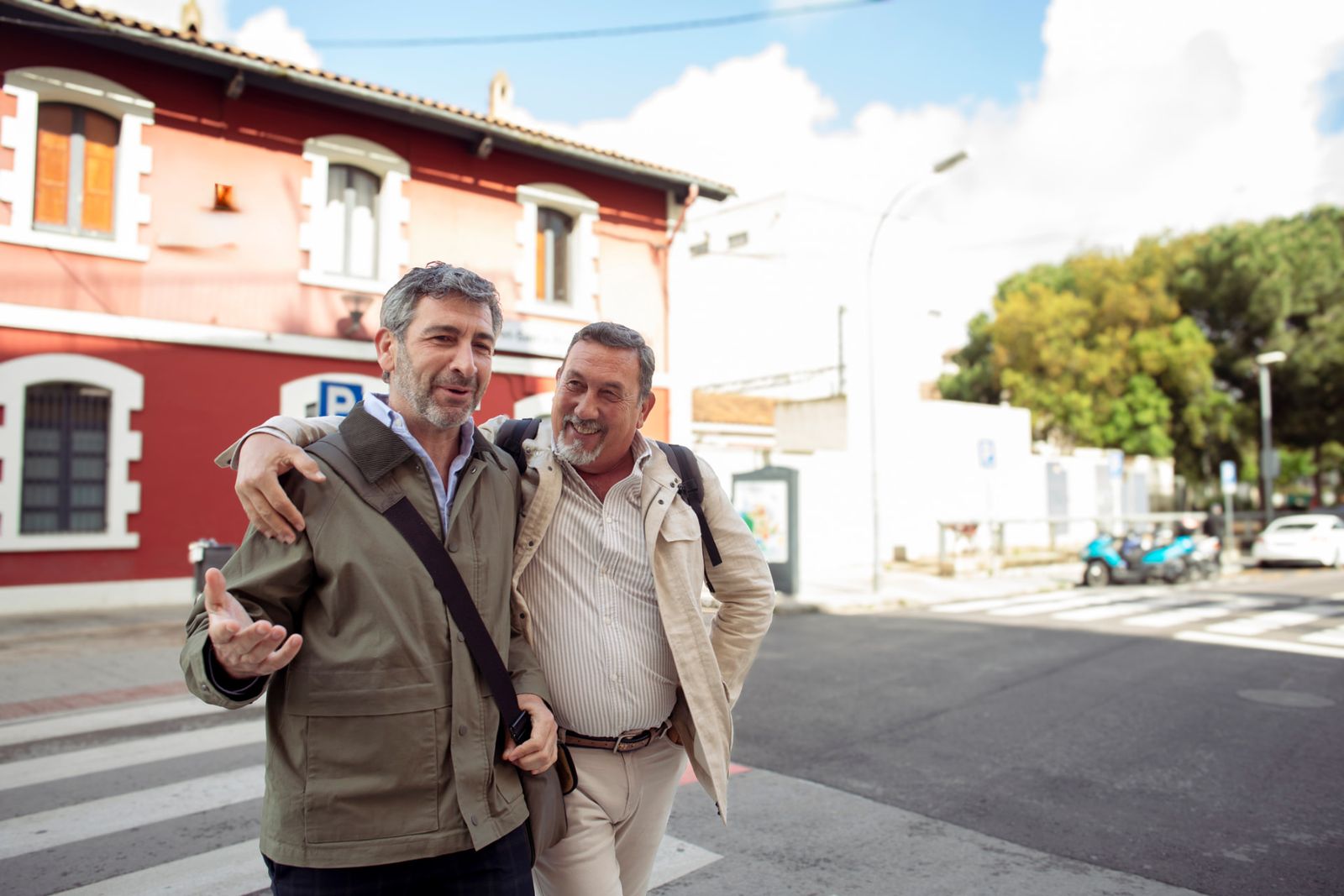 Two men in their fifties walk along a street laughing, one with his arm around the other’s shoulder.